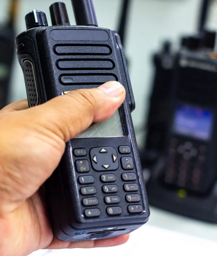 Hand holding a digital two-way radio with keypad, with a second radio in the background