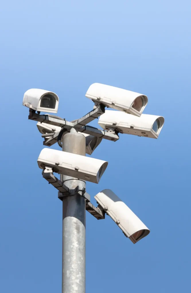 Cluster of six outdoor surveillance cameras mounted on a pole against a clear blue sky