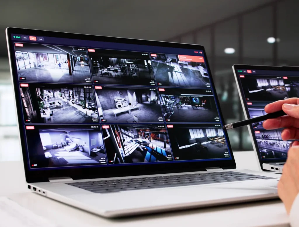 Analyst pointing a stylus at a laptop displaying a grid of live CCTV camera feeds