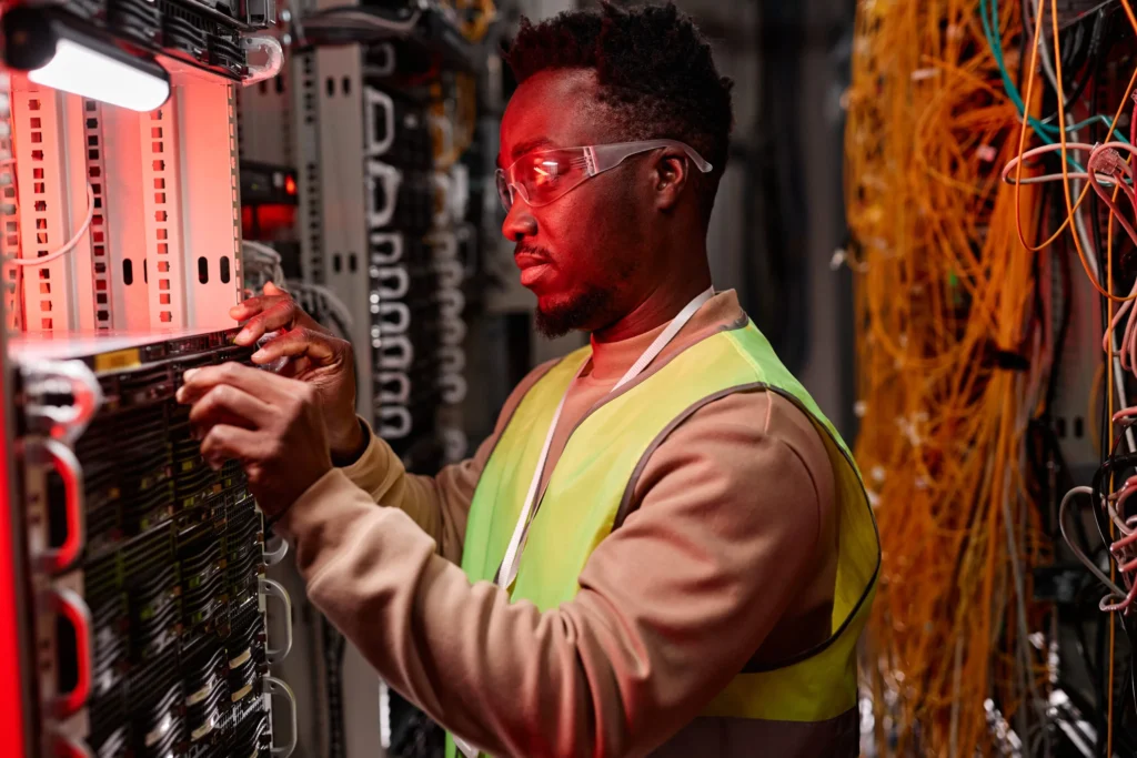 Technician in safety glasses and hi-vis vest servicing a server inside a network equipment rack