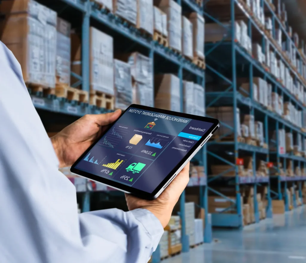 Worker reviewing a warehouse management dashboard on a tablet among stocked warehouse racks