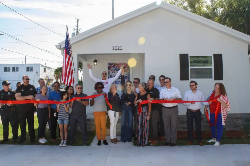 Crowd cutting a red ribbon outside a Hessel Family Foundation Welcome Home house